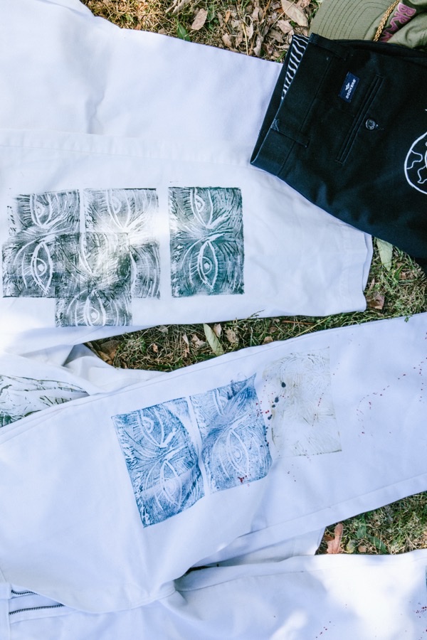 Block-printed eye motifs on reworked white garments, laid out on grass.
